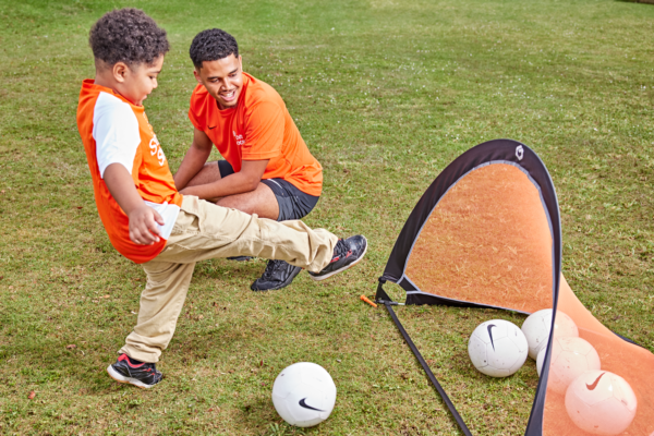 Soccer Shots coach watching a boy kick a goal.